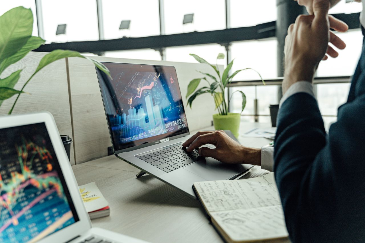 our-story-01 A professional analyzing stock market data on a laptop in a bright office environment.