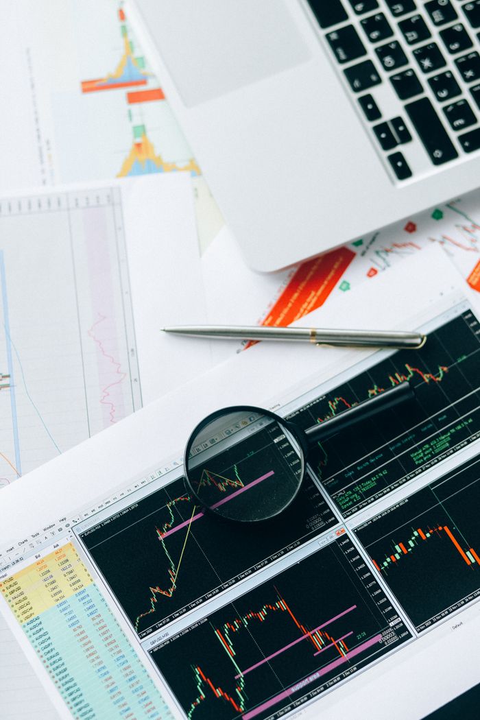 about-07 Magnifying glass and graphs depicting stock market data analysis on paper documents.