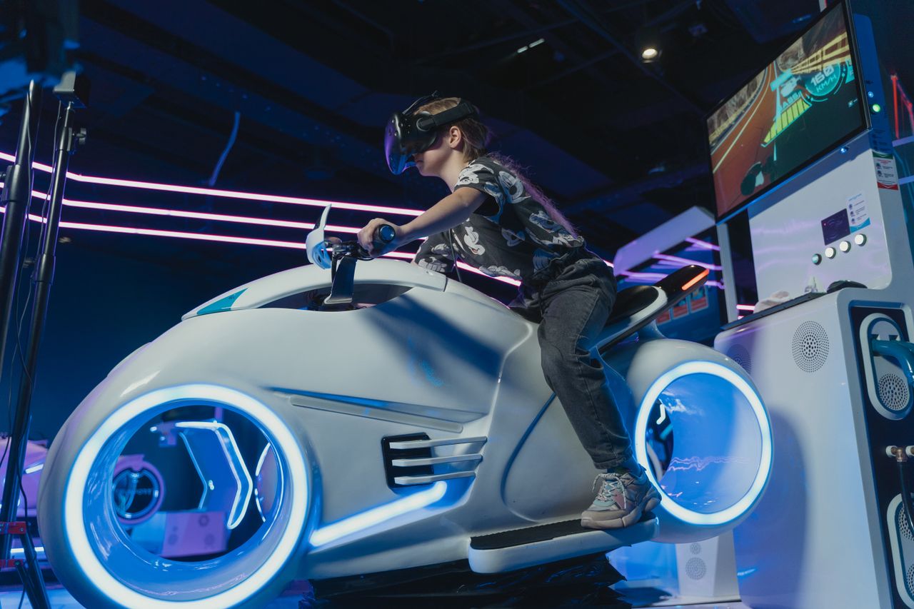 mission-02 A child enjoying a virtual motorcycle ride with VR glasses in an arcade setting.